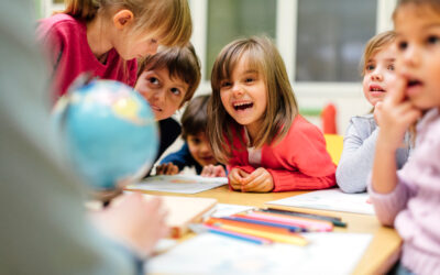 Preschool teacher teaching her children about geography. Using globe and asking the questions. Children sitting by the table and listen teacher carefully. Models in this shot are part of real kindergarten group and their teacher.
