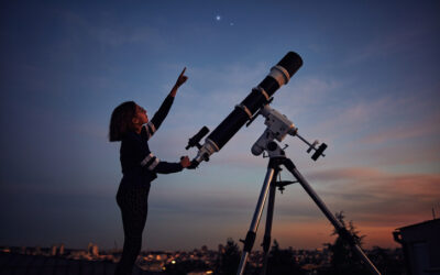 Girl with astronomical telescope stargazing under twilight sky.